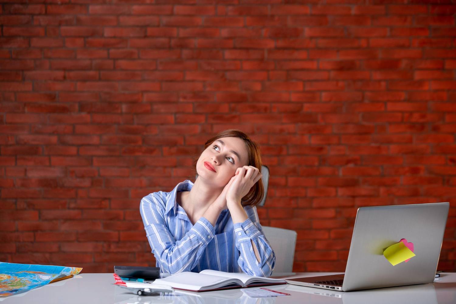 Une femme devant un bureau de travail et un ordinateur portable rêvasse